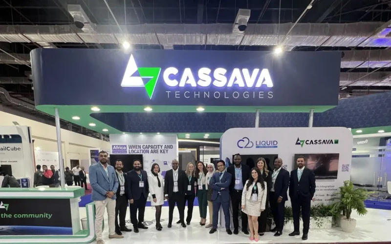 A professional team stands in front of a modern "Cassava Technologies" exhibition booth featuring a green and blue logo, with signs for Liquid Intelligent Technologies and AXON Networks visible in the background.