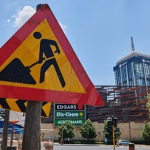 A wide shot of several yellow construction cranes towering over the modern skyline of the Rosebank district in Johannesburg under a bright blue sky