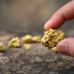 High-quality 3D render of a golden map of Uganda placed on a dark, reflective surface next to several stacked gold bullion bars
