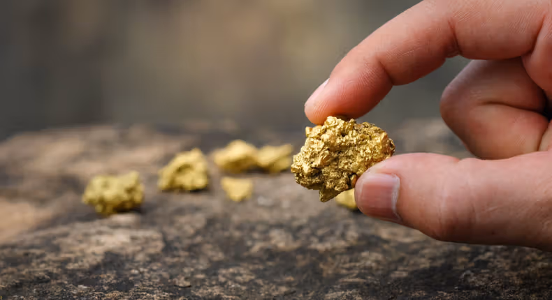 High-quality 3D render of a golden map of Uganda placed on a dark, reflective surface next to several stacked gold bullion bars